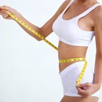 Close up slimming female with beautiful body and measuring her waistline  with measure tape on white background and copy space